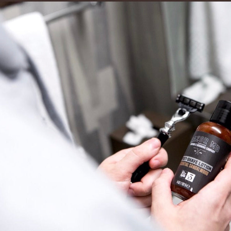 Person holding a bottle RAZOR MD Post shave lotion and a Bk360 razor in a bathroom setting
