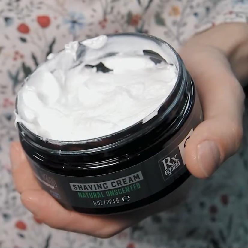Person holding a jar of RAZOR MD Shave cream with a floral-patterned fabric background
